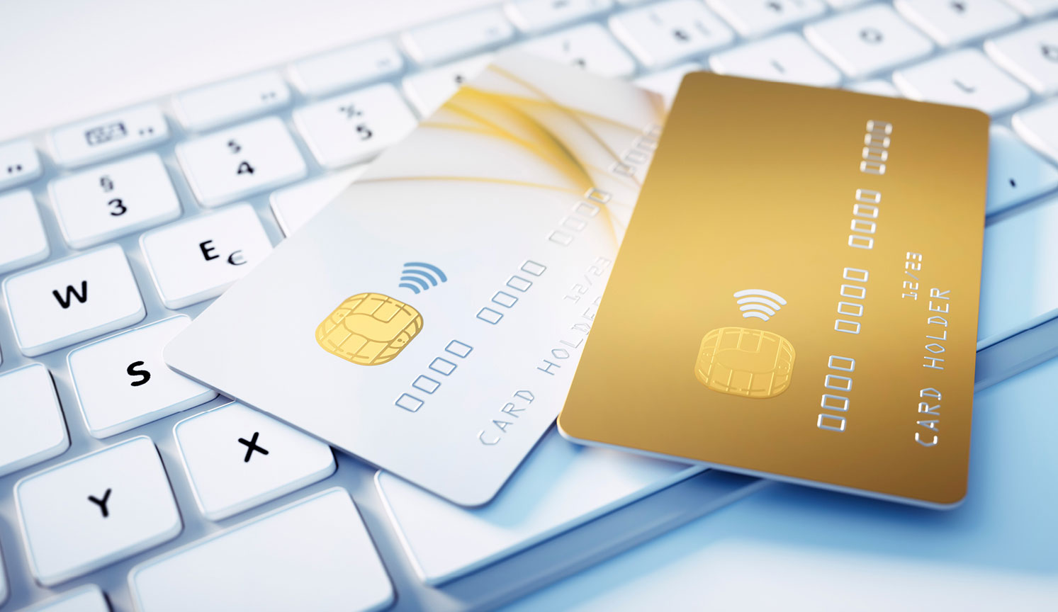 two bank cards, one white and one gold, lying on top of a computer keyboard